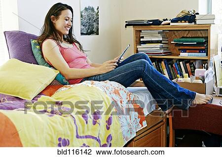 Stock Image - Mixed race college student using tablet computer in dorm. Fotosearch