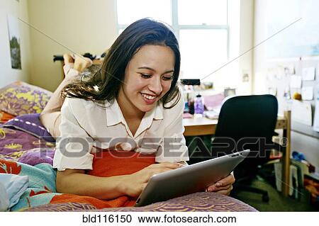 Stock Image - Mixed race college student using tablet computer in dorm. Fotosearch