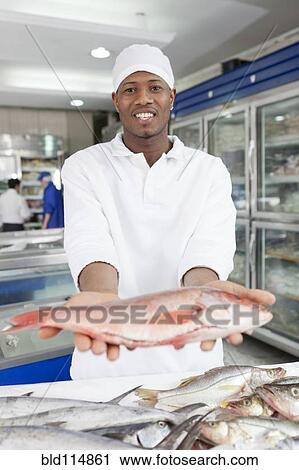 Stock Image - Mixed race grocer preparing fish in market. Fotosearch