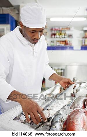 Stock Photo - Mixed race grocer preparing fish in market. Fotosearch