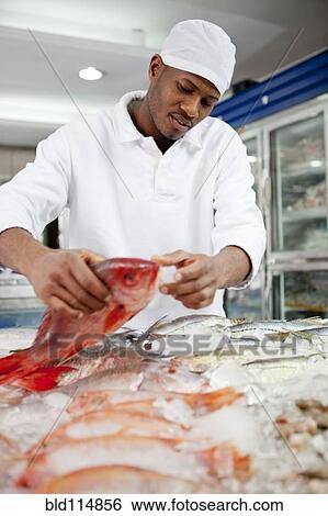 Stock Photograph - Mixed race grocer preparing fish in market. Fotosearch
