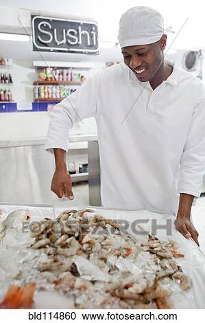 Stock Image - Mixed race grocer preparing seafood in market. Fotosearch