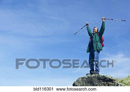Stock Image - Mixed race man hiking on rocky hill. Fotosearch