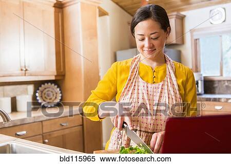 Stock Photography - Mixed race woman cooking in kitchen. Fotosearch