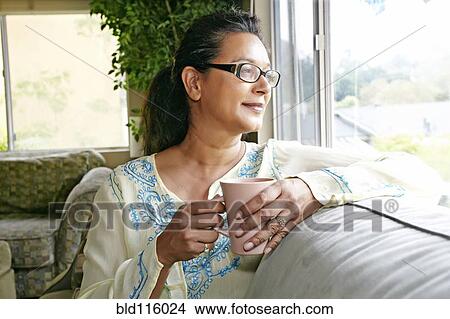 Mixed race woman having cup of coffee on sofa View Large Photo Image Picture - Mixed race woman having cup of coffee on sofa. Fotosearch