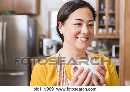 Stock Photo - Mixed race woman having cup of coffee in kitchen. Fotosearch