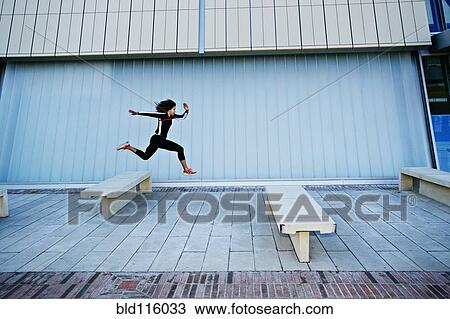 Stock Image - Mixed race woman running on city street. Fotosearch