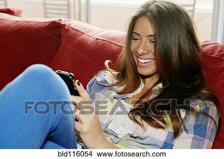 Mixed race woman using cell phone on sofa View Large Photo Image Picture - Mixed race woman using cell phone on sofa. Fotosearch