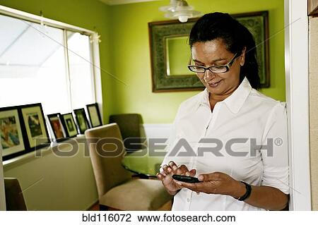 Stock Image - Mixed race woman using cell phone indoors. Fotosearch