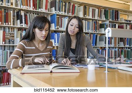 Stock Image - Students working at desk in library. Fotosearch