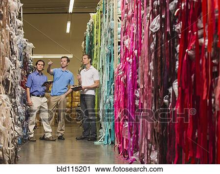 Stock Image - Workers examining fabric in textile factory. Fotosearch