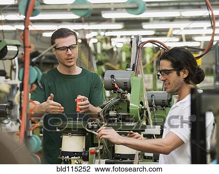 Stock Image - Workers operating machinery in textile factory. Fotosearch