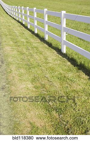 Stock Image - A long white farm fence in countryside surrounding pasture. Fotosearch