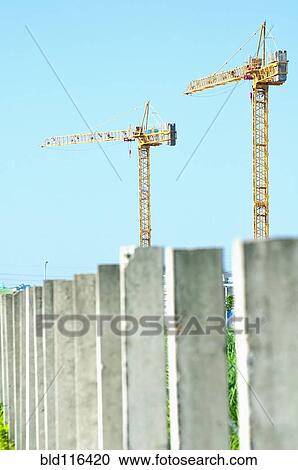 Stock Image - Two construction cranes above a row of concrete pillars. Fotosearch