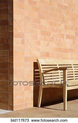Stock Image - Wooden Bench Against Corner of Brick Building. Fotosearch