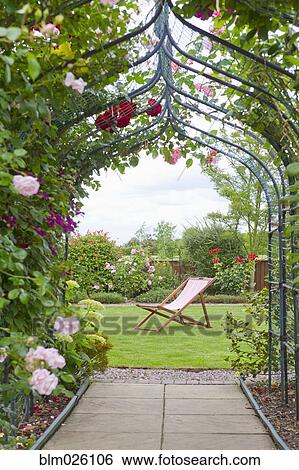 Stock Photograph - A garden with a rose arch, and a deck chair. Fotosearch