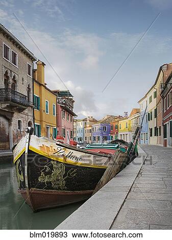 Stock Image - Boat in a Canal Lined With Colorful Homes. Fotosearch