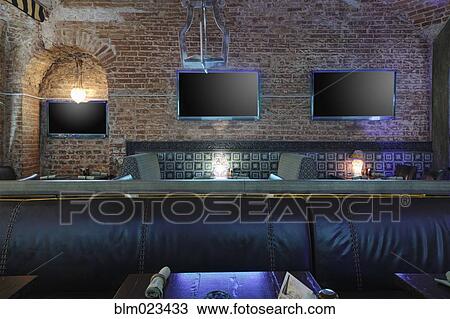 Stock Image - Three TV screens on brick wall in restaurant behind leather seat. Fotosearch