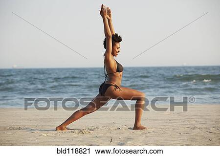 Stock Image - Black woman practicing yoga on beach. Fotosearch