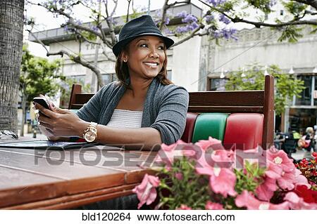 Black woman using cell phone at sidewalk cafe View Large Photo Image Picture - Black woman using cell phone at sidewalk cafe. Fotosearch