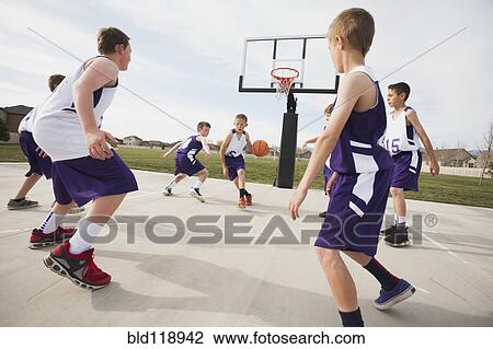 Stock Image - Caucasian boys playing basketball on court. Fotosearch
