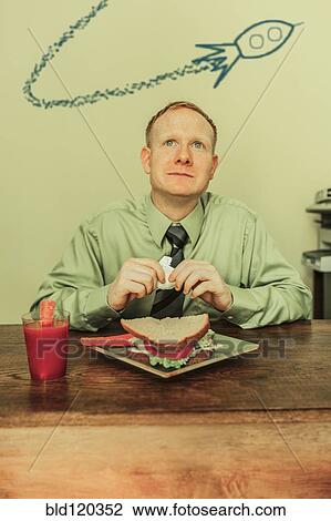 Stock Image - Caucasian businessman eating lunch with spaceship overhead. Fotosearch