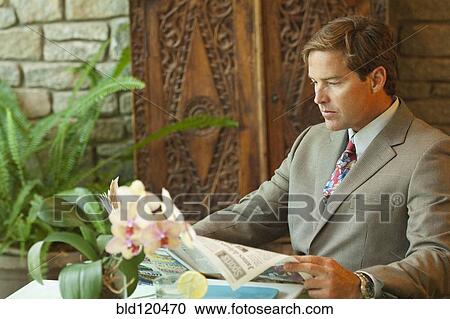 Stock Image - Caucasian businessman reading newspaper on patio. Fotosearch