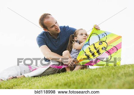 Stock Photo - Caucasian father and daughter fixing kite in grass. Fotosearch