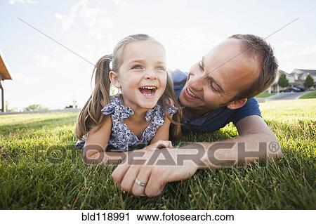 Stock Image - Caucasian father and daughter laying in grass. Fotosearch