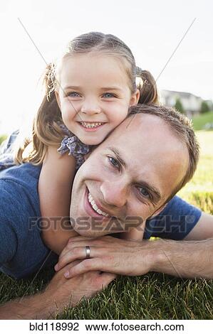 Stock Image - Caucasian father and daughter laying in grass. Fotosearch