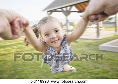Stock Photograph - Caucasian father spinning daughter in park. Fotosearch