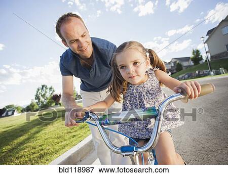 Stock Photo - Caucasian father teaching daughter to ride bicycle. Fotosearch