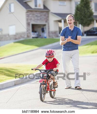 Caucasian father teaching son to ride bicycle View Large Photo Image Picture - Caucasian father teaching son to ride bicycle. Fotosearch