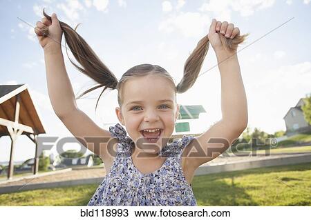 Stock Image - Caucasian girl playing with pigtails outdoors. Fotosearch