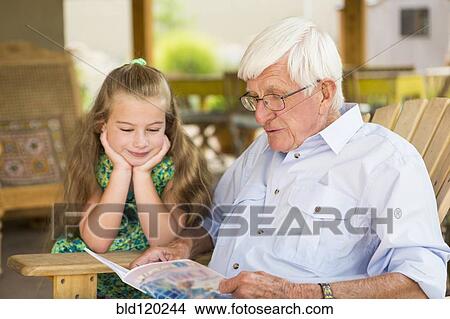 Picture - Caucasian man and granddaughter reading outdoors. Fotosearch