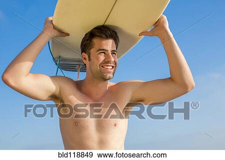 Stock Photo - Caucasian man carrying surfboard. Fotosearch