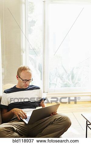 Caucasian man using laptop on sofa View Large Photo Image Stock Photo - Caucasian man using laptop on sofa. Fotosearch