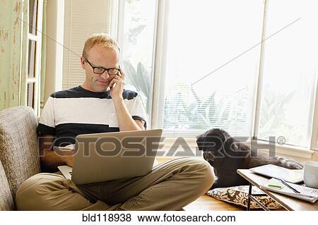 Stock Photo - Caucasian man using laptop on sofa. Fotosearch