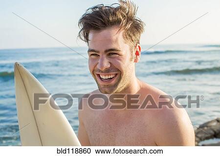Stock Image - Caucasian man with surfboard on beach. Fotosearch