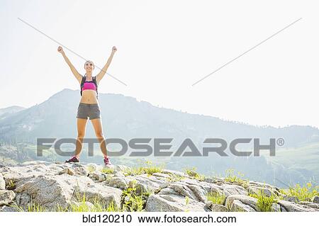 Stock Image - Caucasian woman cheering on rocky hilltop. Fotosearch