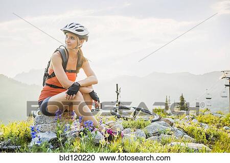 Stock Image - Caucasian woman sitting near mountain bike. Fotosearch