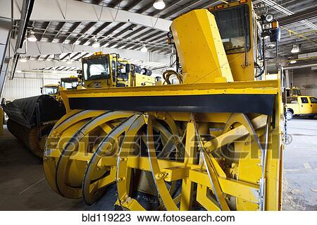 Stock Image - Close up of snowplow parked in warehouse. Fotosearch