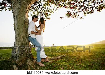 Picture - Couple hugging by tree in park. Fotosearch