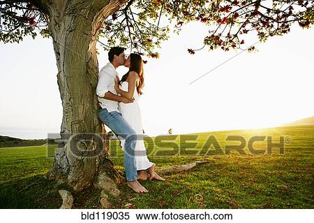 Couple kissing by tree in park View Large Photo Image Stock Photography - Couple kissing by tree in park. Fotosearch