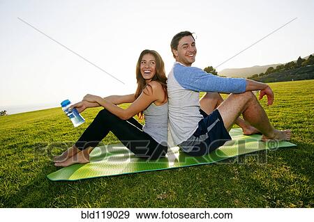 Stock Photo - Couple sitting on yoga mat in park. Fotosearch