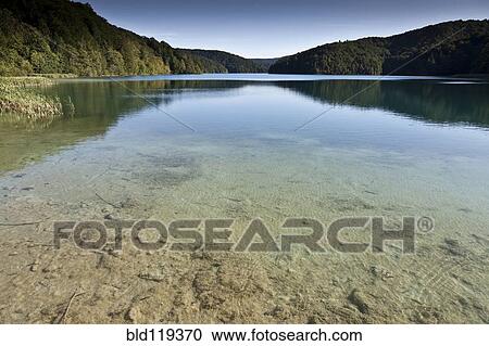 Stock Image - Hills and sky reflected in still lake. Fotosearch