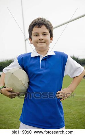 Stock Image - Hispanic boy holding rugby ball on field. Fotosearch