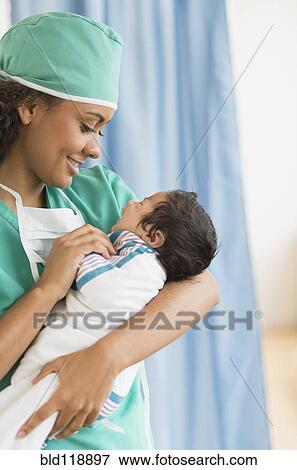 Stock Photo - Hispanic doctor holding newborn in hospital. Fotosearch