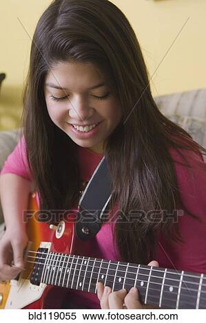 Stock Photography - Hispanic girl playing guitar on sofa. Fotosearch
