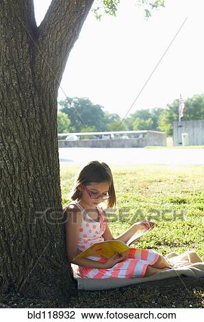 Stock Image - Hispanic girl reading in park. Fotosearch